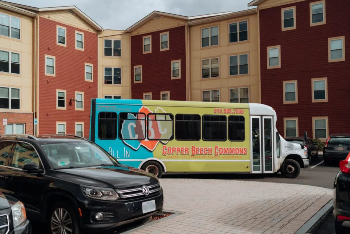 Colorful bus parked near apartment buildings exterior at Copper Beech Commons Student Housing in Syracuse Student Accommodation