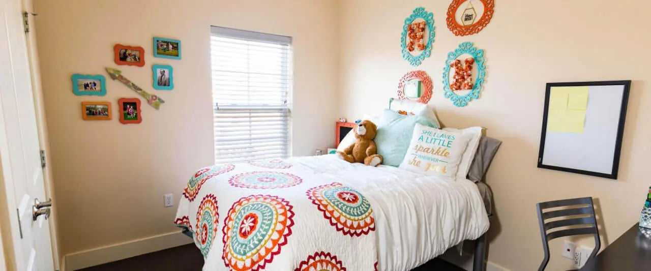 Bed with colorful quilt teddy bear photos whiteboard bedroom at Beacon Commons in Springfield Student Accommodation
