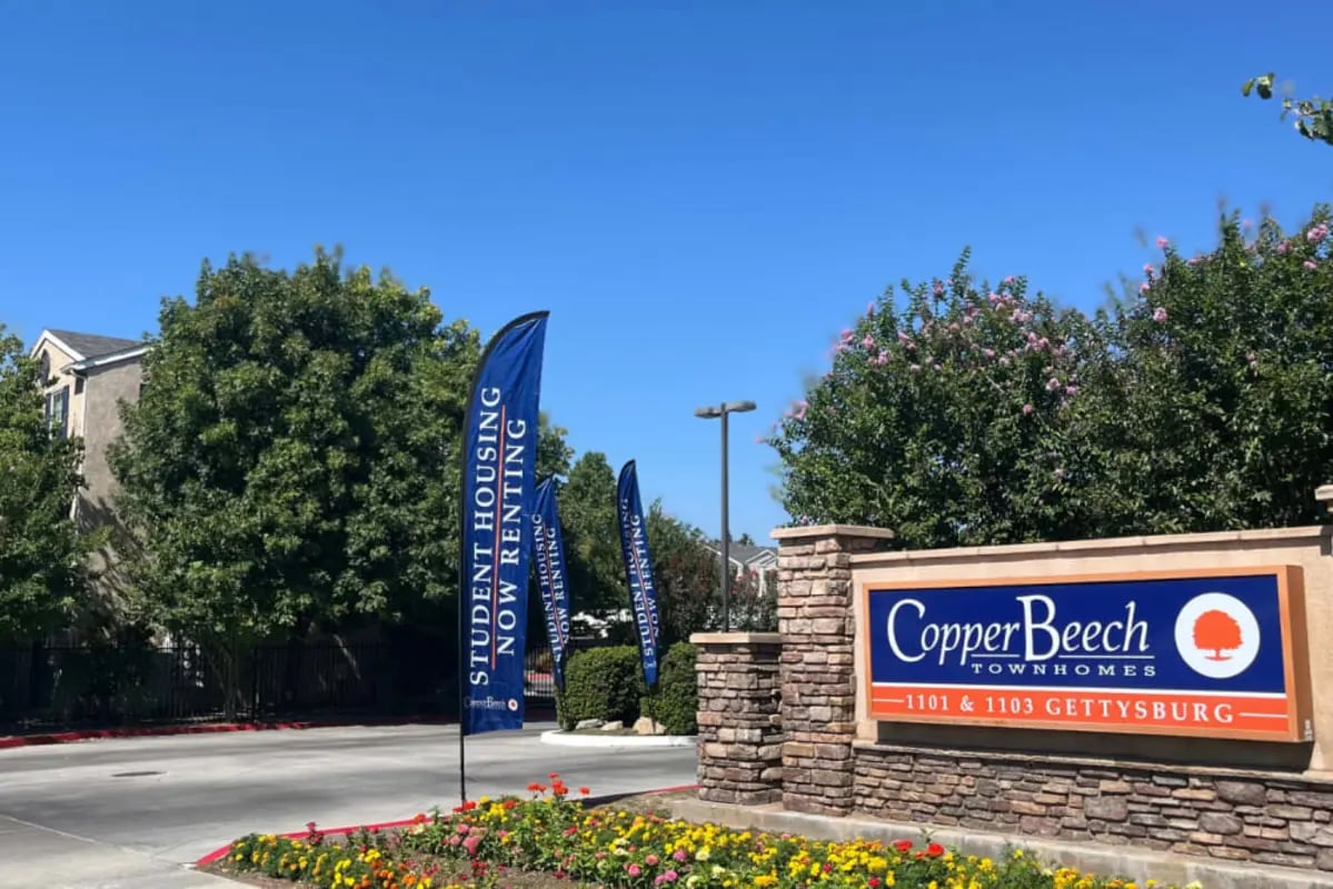 Entrance sign with flags and flowers exterior at Copper Beech Townhomes in Clovis Student Accommodation