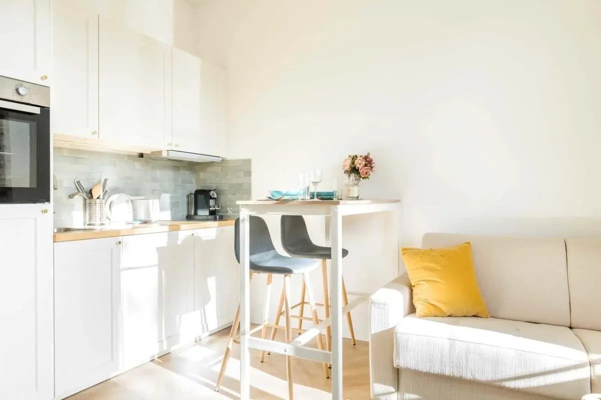 White cabinets table chairs sofa yellow cushion living kitchen at Apartment in 8 Rue Verderet, 75016 Paris, France in Paris Student Accommodation