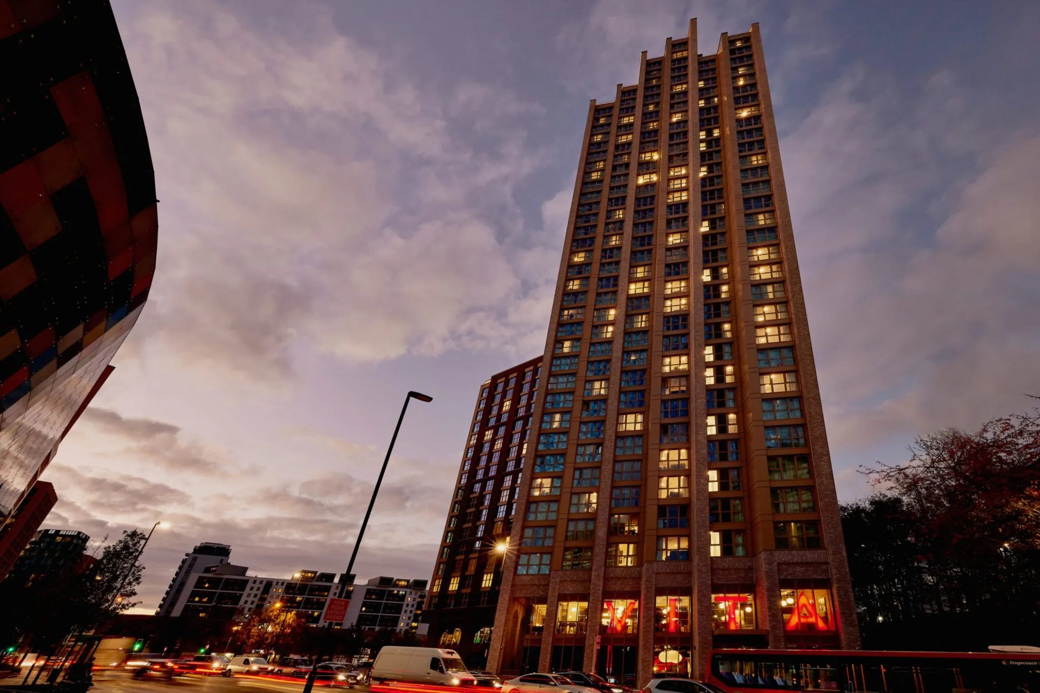 Tall apartment building lit windows busy street exterior at Vita Student Lewisham Exchange in London Student Accommodation