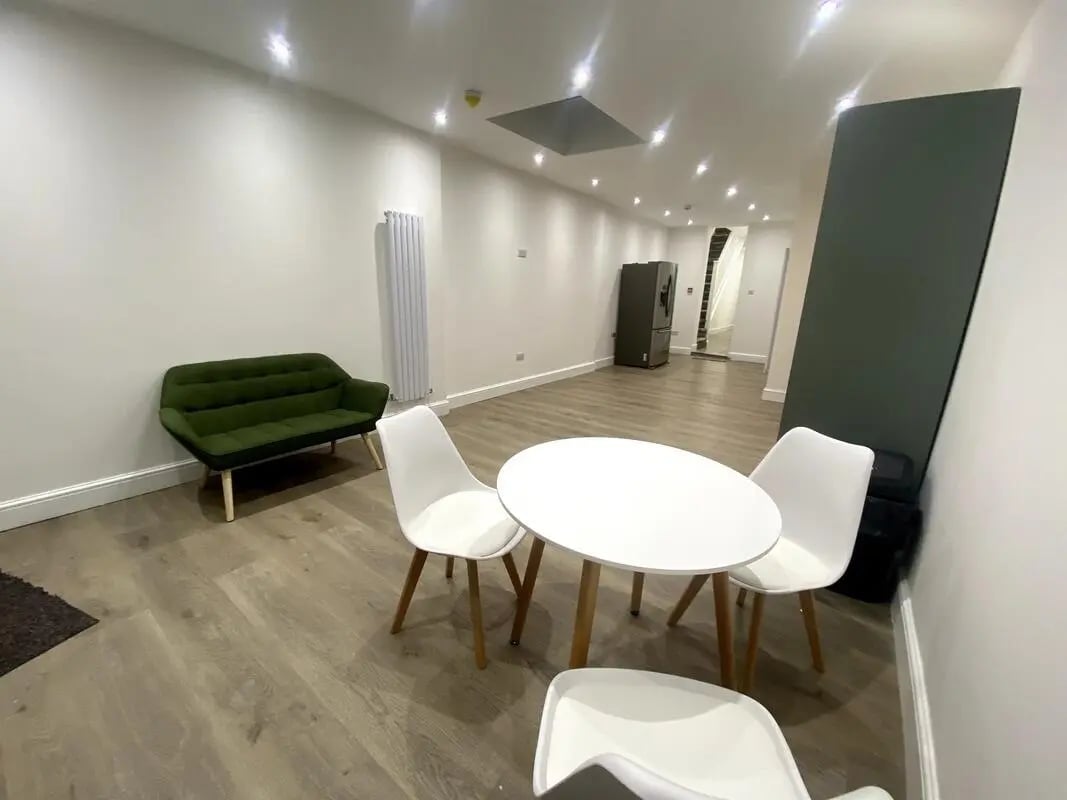 Green sofa white table chairs refrigerator living area at E7 8PF, Shaftsbury Rd, London in London Student Accommodation