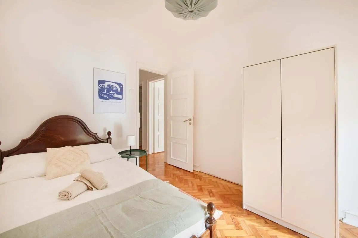 Bed with wooden headboard closet doors and artwork Bedroom at Bedroom with balcony in a 6-bedroom apartment in Lisbon - Room 1 in Lisbon Student Accommodation