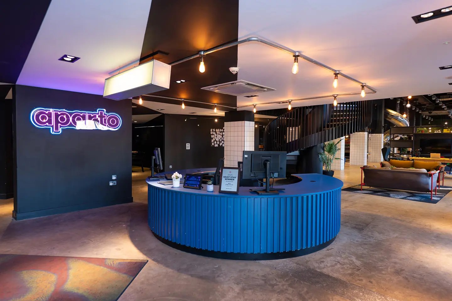 Blue reception desk with computers and neon sign common area exterior at aparto Glasgow West End in Glasgow Student Accommodation