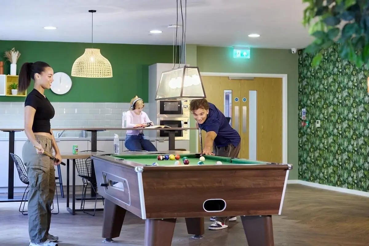 Pool table with players and kitchen area recreation area at Gulson Gardens in Coventry Student Accommodation