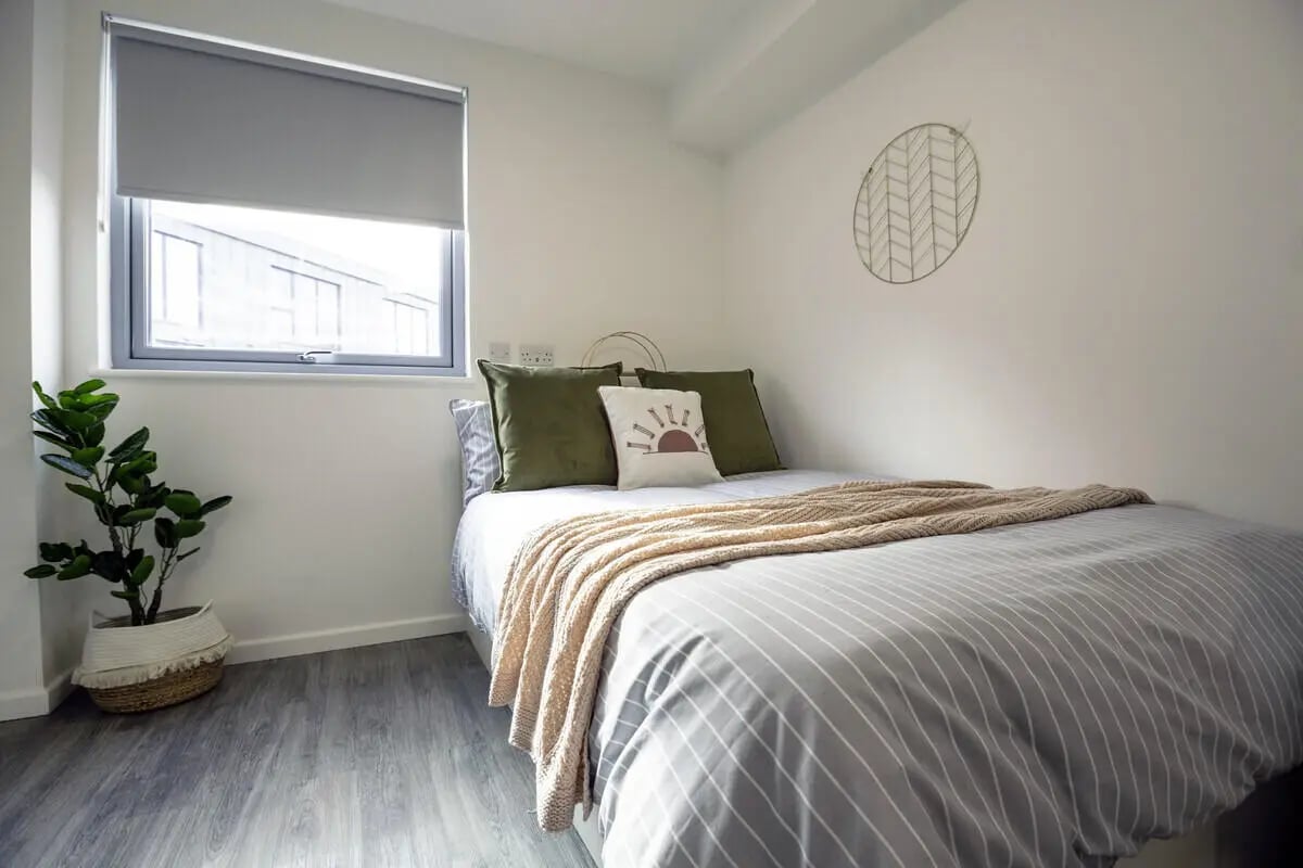 Bed with striped duvet green pillows wall art bedroom at Westcombe House in London Student Accommodation