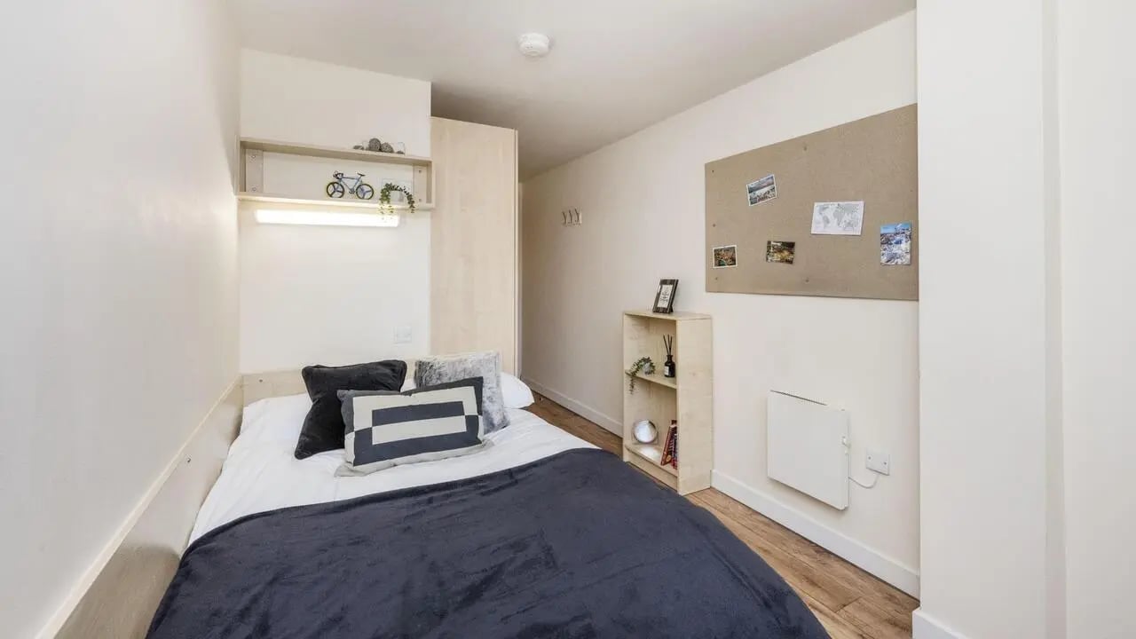 Bed with dark duvet shelf and corkboard Bedroom at Rockingham House in Sheffield Student Accommodation