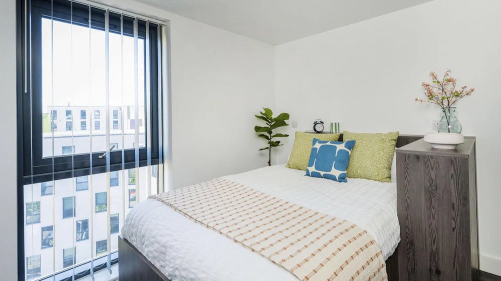 Bed with pillows plant alarm clock and vase bedroom at Opto Newcastle in Newcastle Upon Tyne Student Accommodation