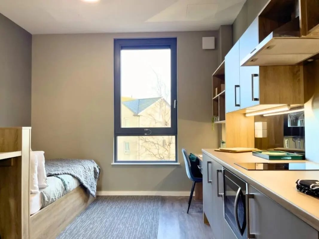 Bed with grey blanket desk with chair kitchen area studio at Justice Mill Studios in Aberdeen Student Accommodation