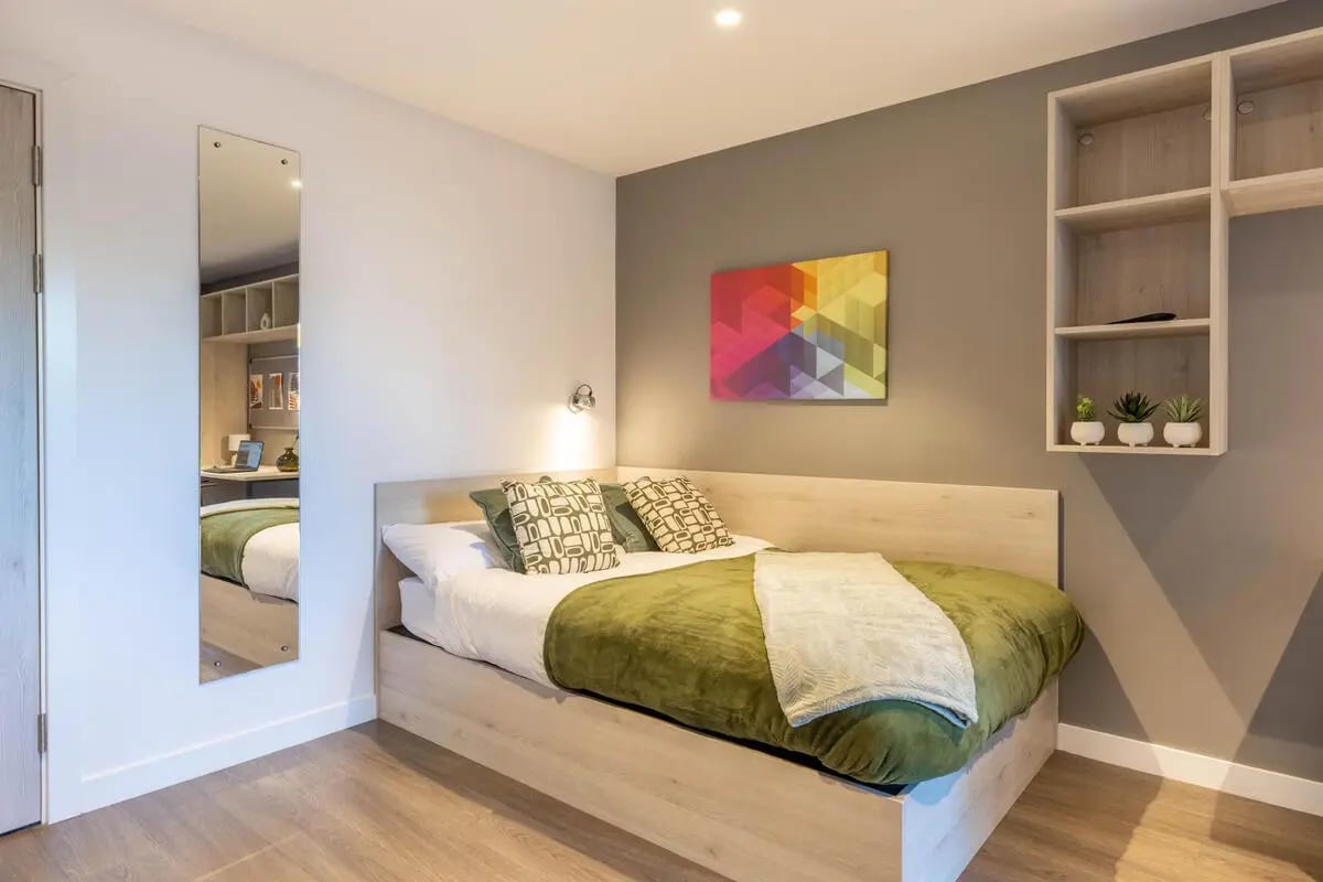 Bed with pillows green blanket art shelves bedroom at Abeleven in Aberdeen Student Accommodation
