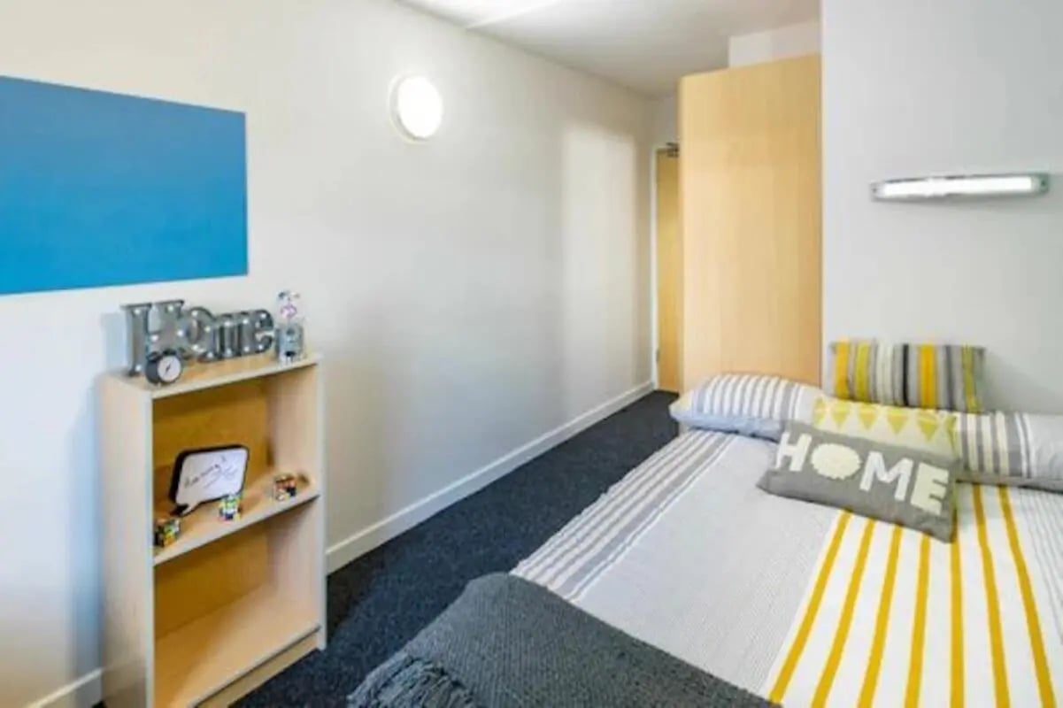 Bed with pillows bookshelf and blue wall art bedroom at Leighton Hall in Preston Student Accommodation