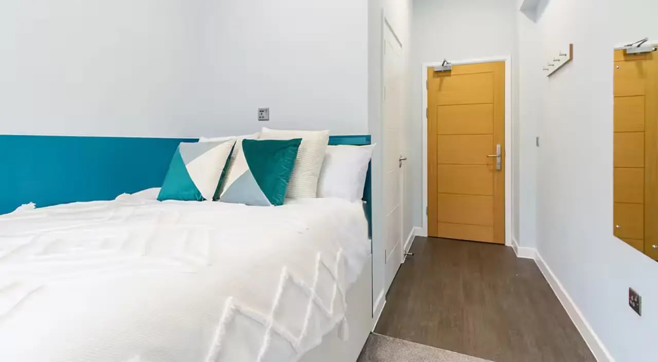 Bed with teal pillows wooden door mirror bedroom at Urban Student Village in Coventry Student Accommodation