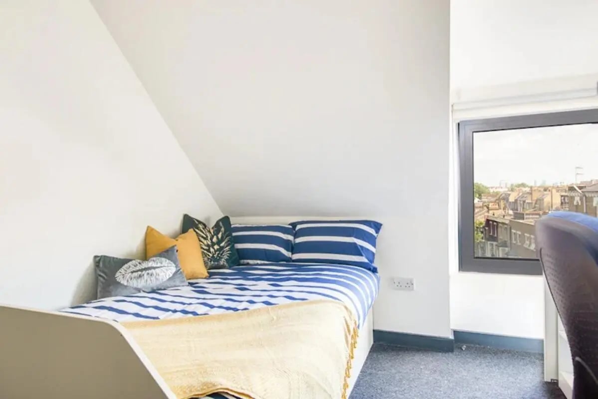 Bed with striped bedding decorative pillows and yellow throw bedroom at Fulham Palace Studios in London Student Accommodation
