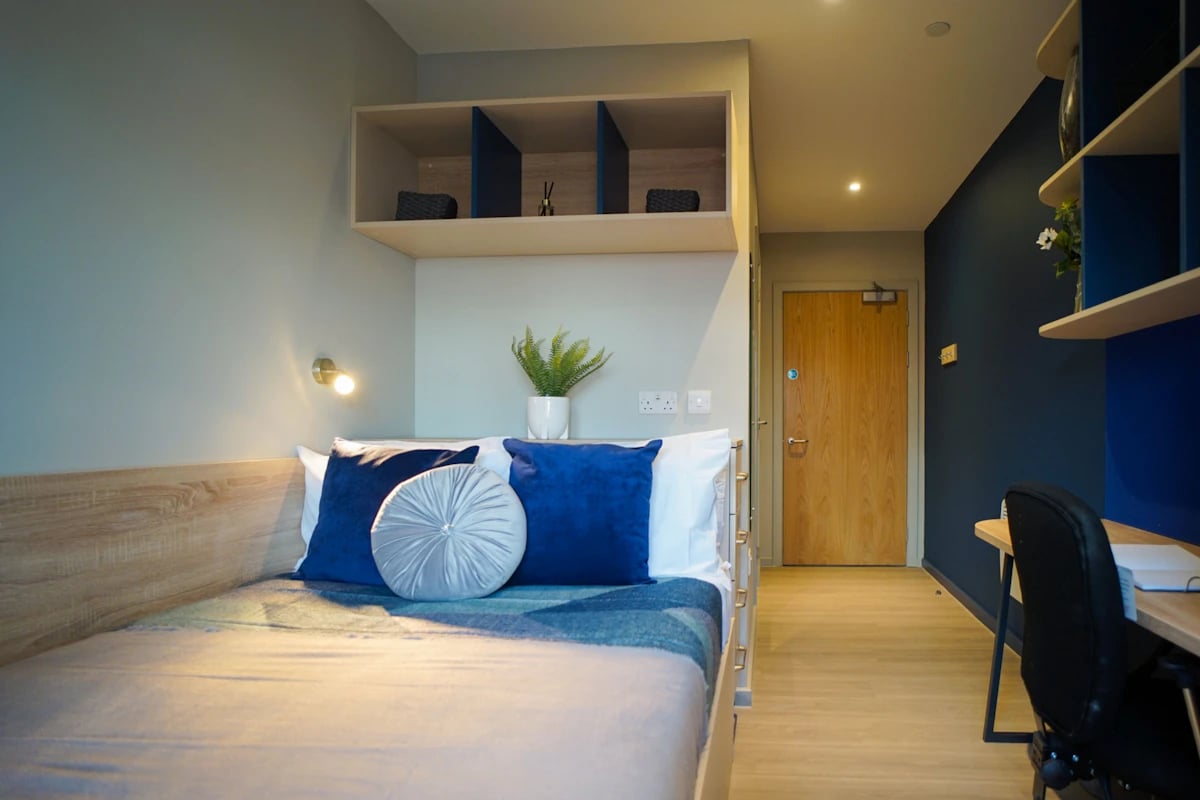 Bed with blue pillows desk and door Bedroom at Straits Meadows in Edinburgh Student Accommodation