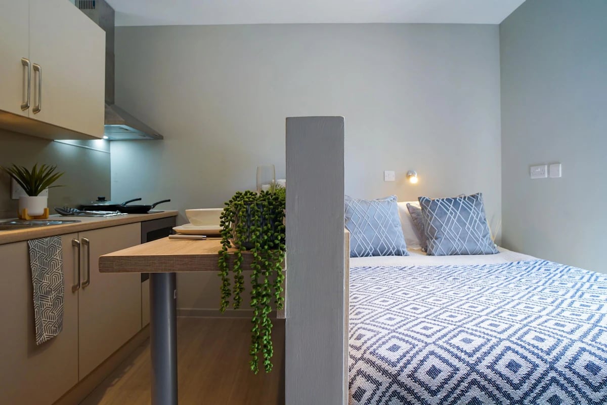Kitchenette and bed with blue pillows and throw. at Straits Meadows in Edinburgh Student Accommodation