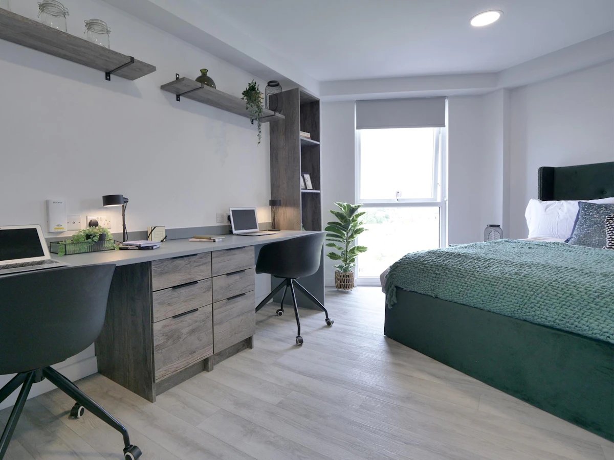 Two desks laptops chairs bed and plant bedroom at Urban Hub in Preston Student Accommodation