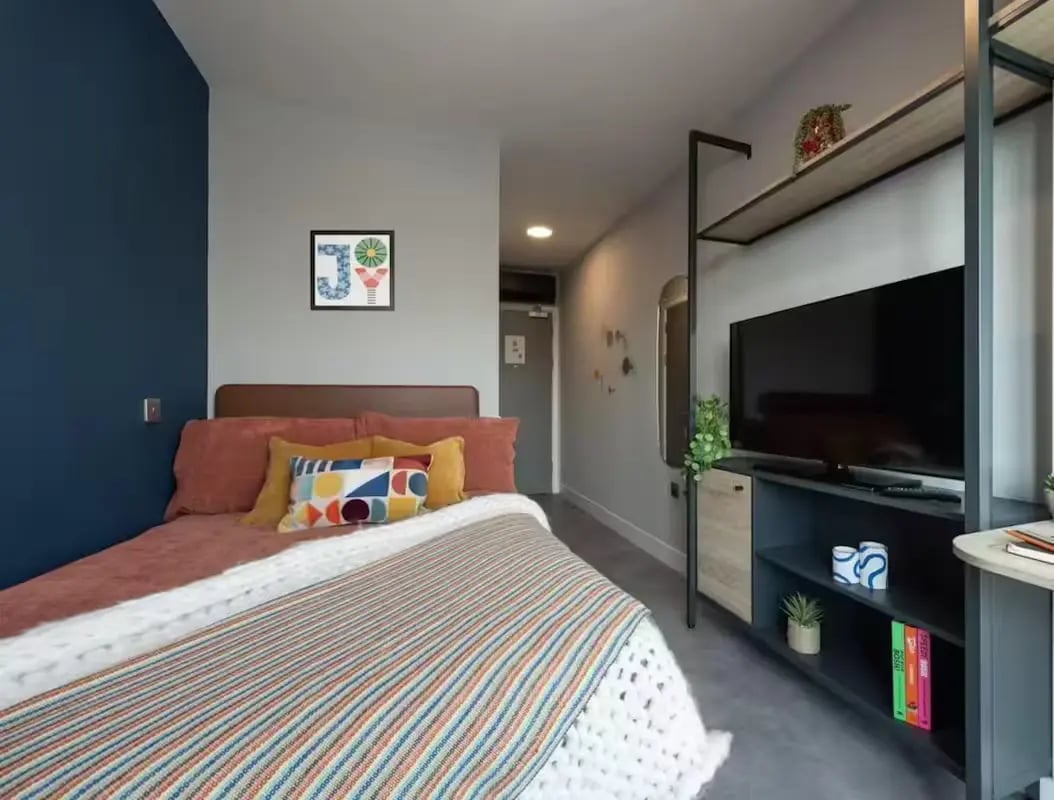 Bed with colorful pillows television and shelves bedroom at The Vantage in Nottingham Student Accommodation