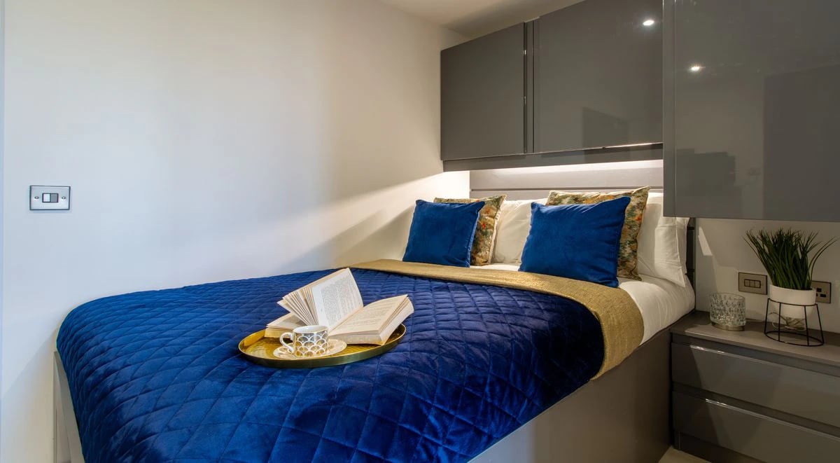 Bed with blue pillows books cup and plant bedroom at The Residence in Coventry Student Accommodation