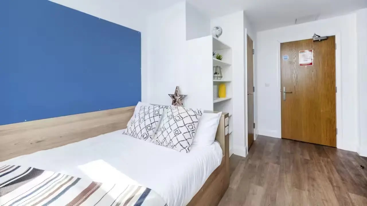Bed with pillows blue wall shelves and door Bedroom at St Leonard's House in Lancaster Student Accommodation