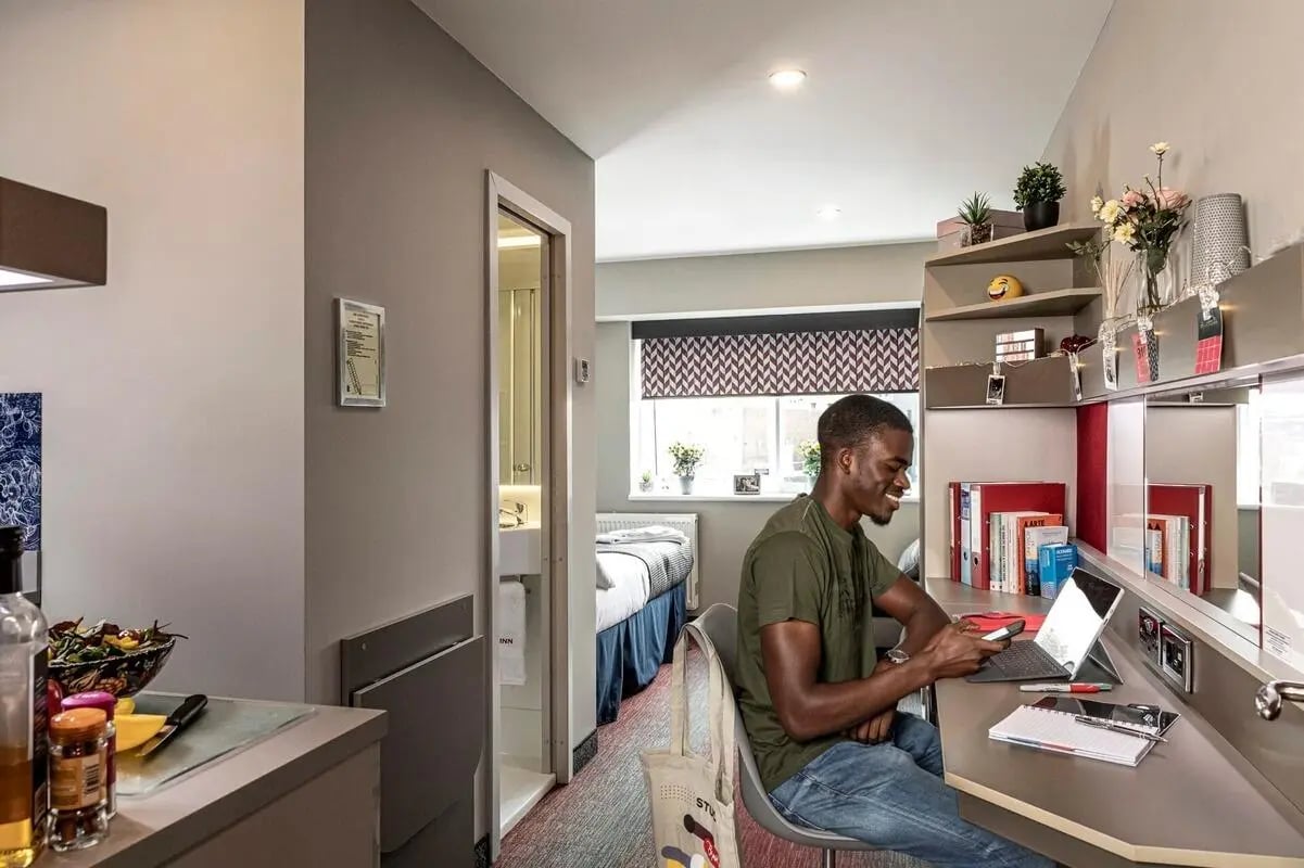 Student working at desk with laptop and bed beyond bedroom at Study Inn Talbot Street Nottingham in Nottingham Student Accommodation