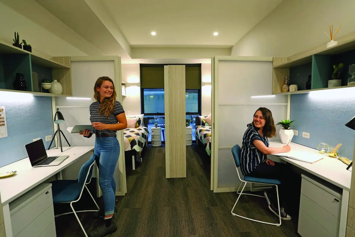 Two students at desks with laptops and beds beyond at Scape Adelaide University in Adelaide Student Accommodation
