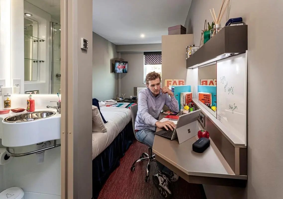 Student studying at desk beside bed and sink study area at Study Inn Talbot Street Nottingham in Nottingham Student Accommodation