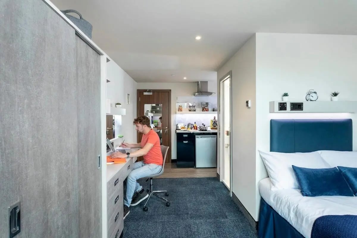 Student studying at desk with kitchen and bed. at Triumph House in Nottingham Student Accommodation