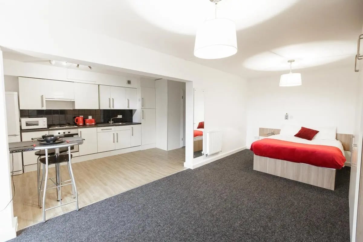 Kitchen and bed with red bedding student studio at AXO Camden in London Student Accommodation