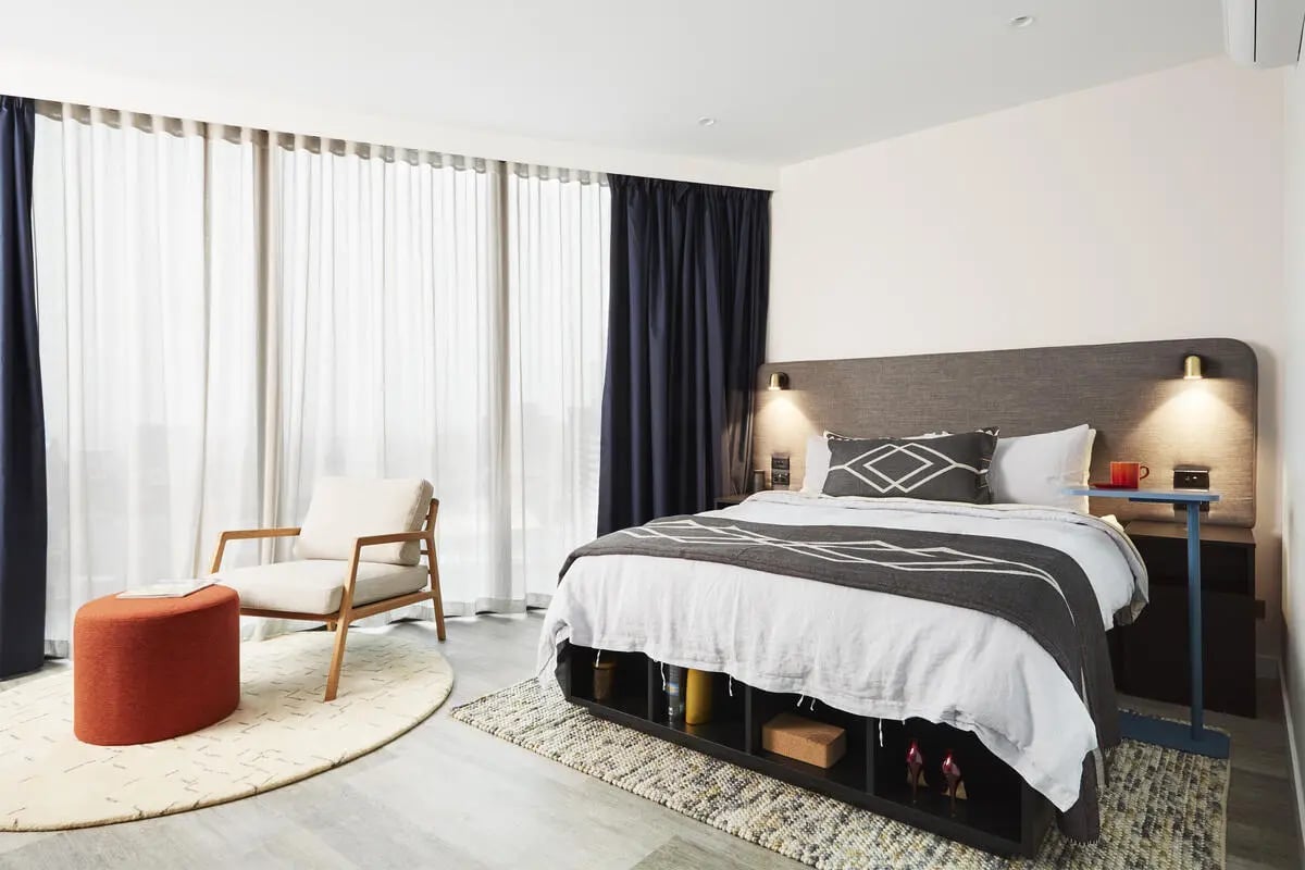 Bed ottoman chair rug and curtains bedroom at Scape Aurora in Melbourne Student Accommodation