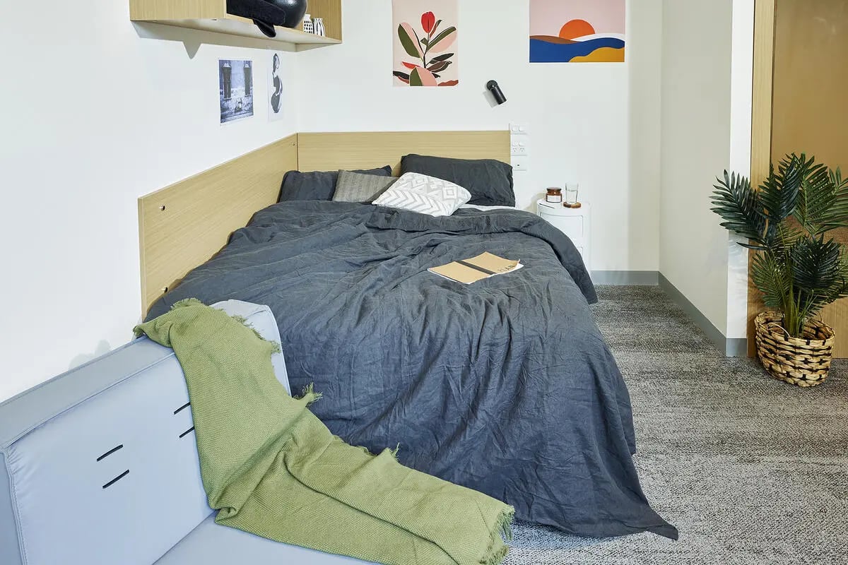 Bed with green throw sofa and plant bedroom at Scape Queensberry in Melbourne Student Accommodation