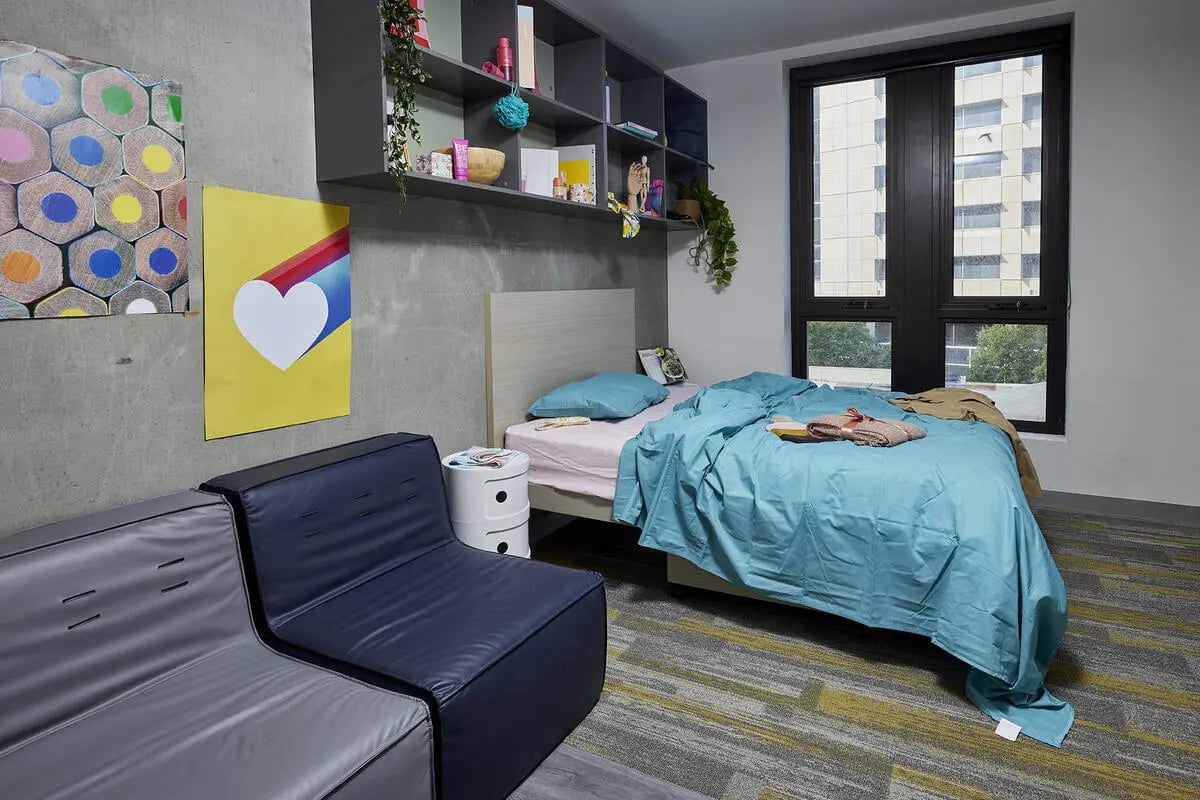 Bed couch shelves window and posters bedroom at Scape Berkeley 2 in Melbourne Student Accommodation