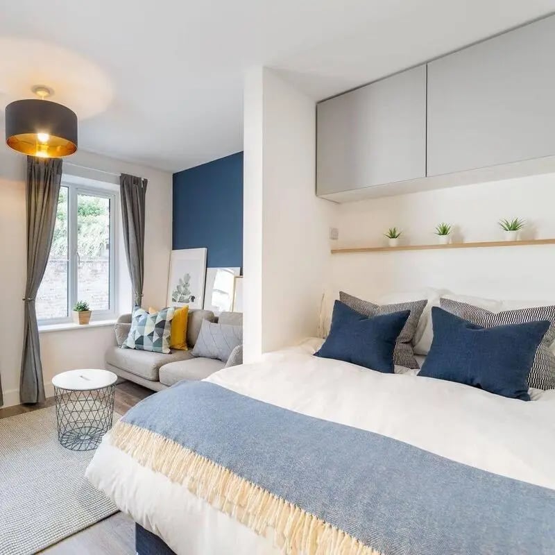 Bed with blue pillows couch small table bedroom living area at Blockyard Apartments in Exeter Student Accommodation