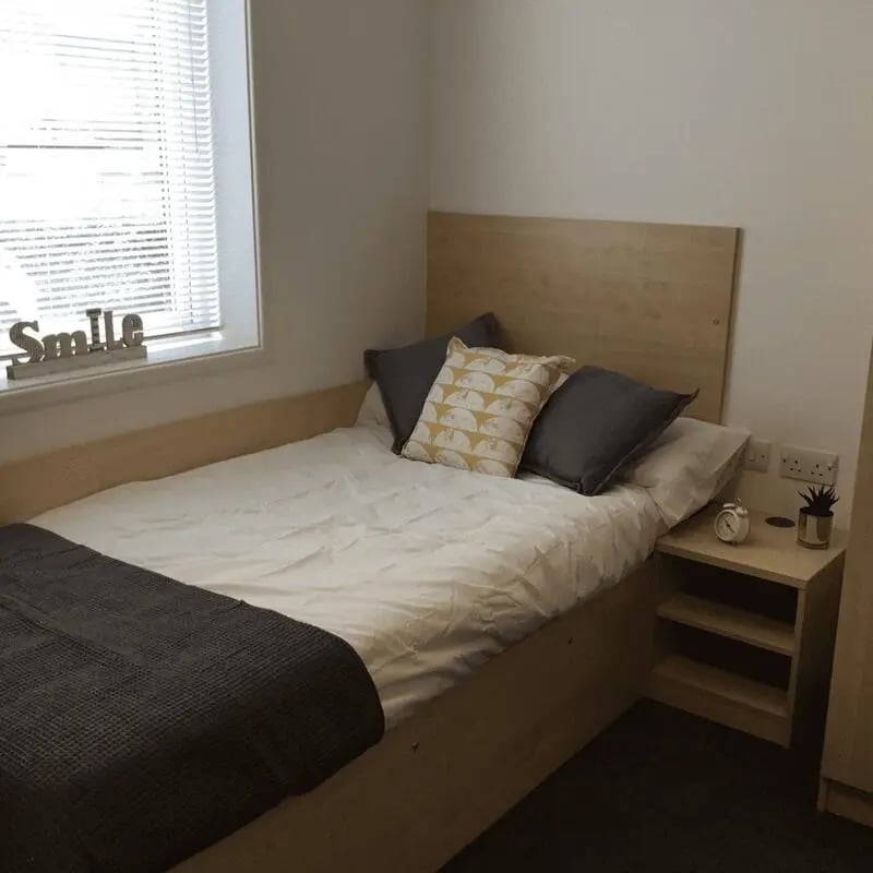Bed with pillows bedside table and window Bedroom at Denton Holme in Carlisle Student Accommodation