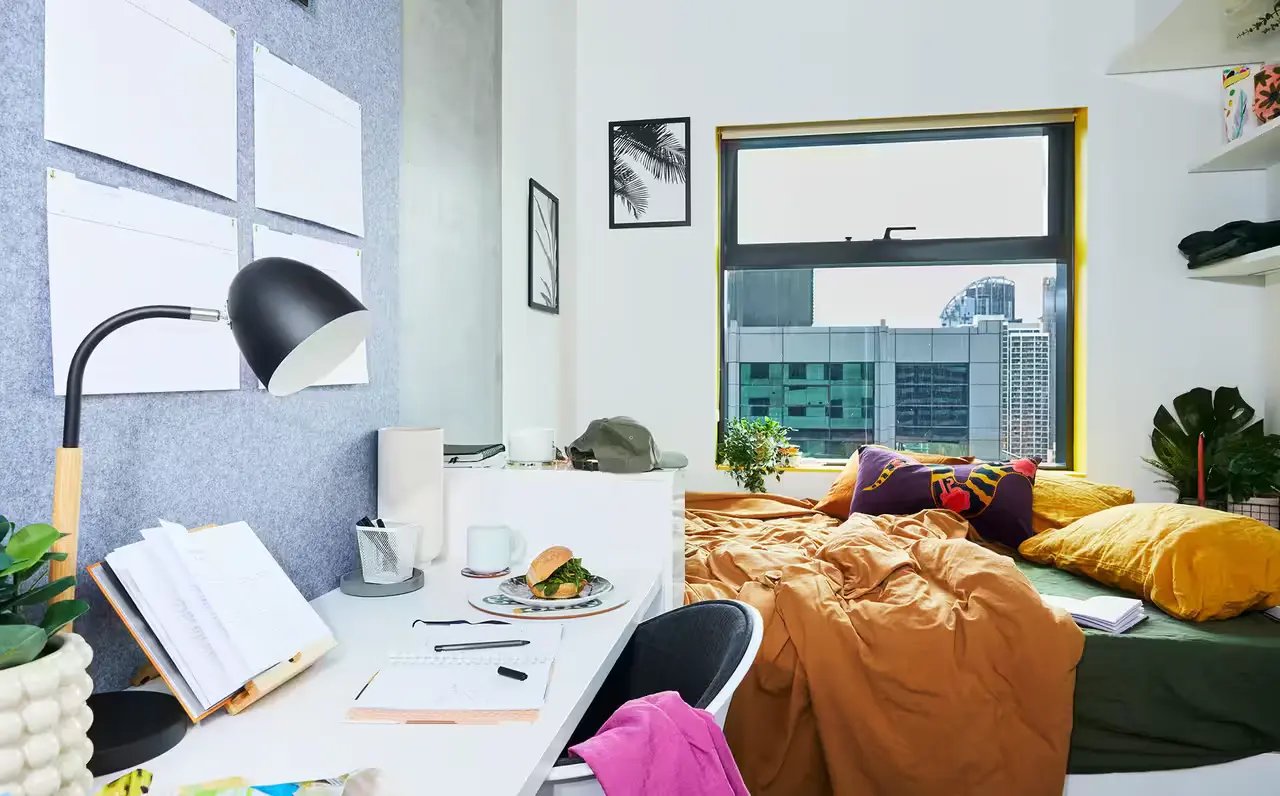 Desk lamp bed pillows and notebooks bedroom study area at Scape Franklin in Melbourne Student Accommodation