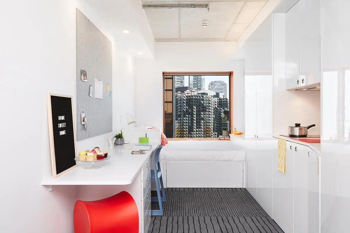 Desk bed kitchen area with city view studio room at Scape Swanston in Melbourne Student Accommodation