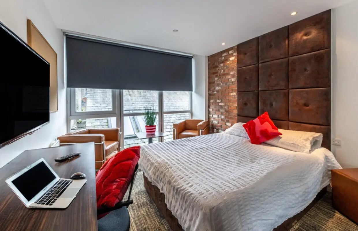 Bed with red pillows leather chairs bedside table and laptop bedroom at Bauhaus Student Langstane Place in Aberdeen Student Accommodation