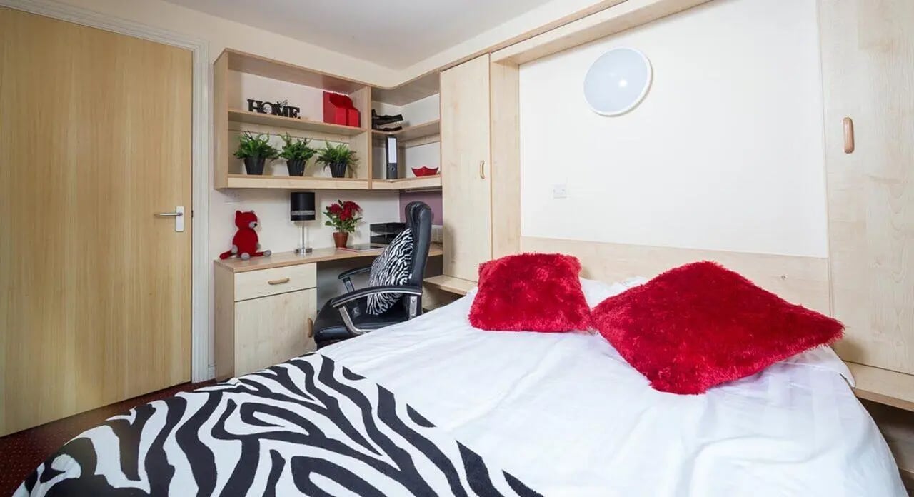 Bed desk chair red pillows bedroom at Q3 Apartments in Manchester Student Accommodation