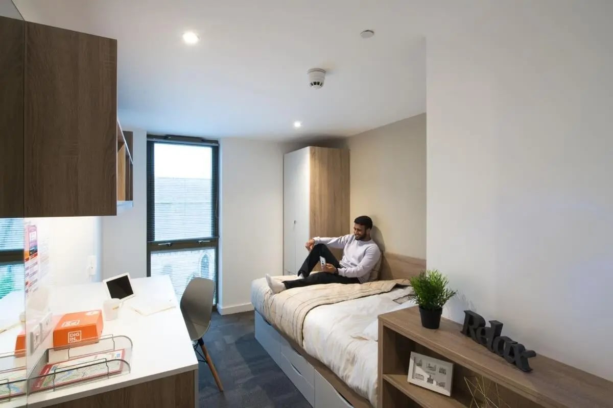 Man on bed with desk and wardrobe bedroom at CityBlock Marton Street in Lancaster Student Accommodation