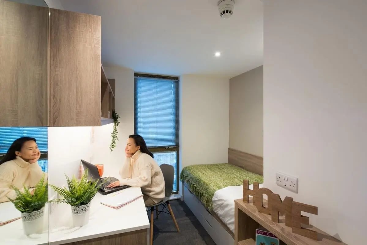 Woman at desk with laptop and bed study area at CityBlock Marton Street in Lancaster Student Accommodation
