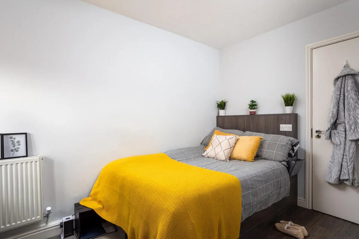 Bed with yellow throw and pillows bedroom at Royal Park Road in Leeds Student Accommodation
