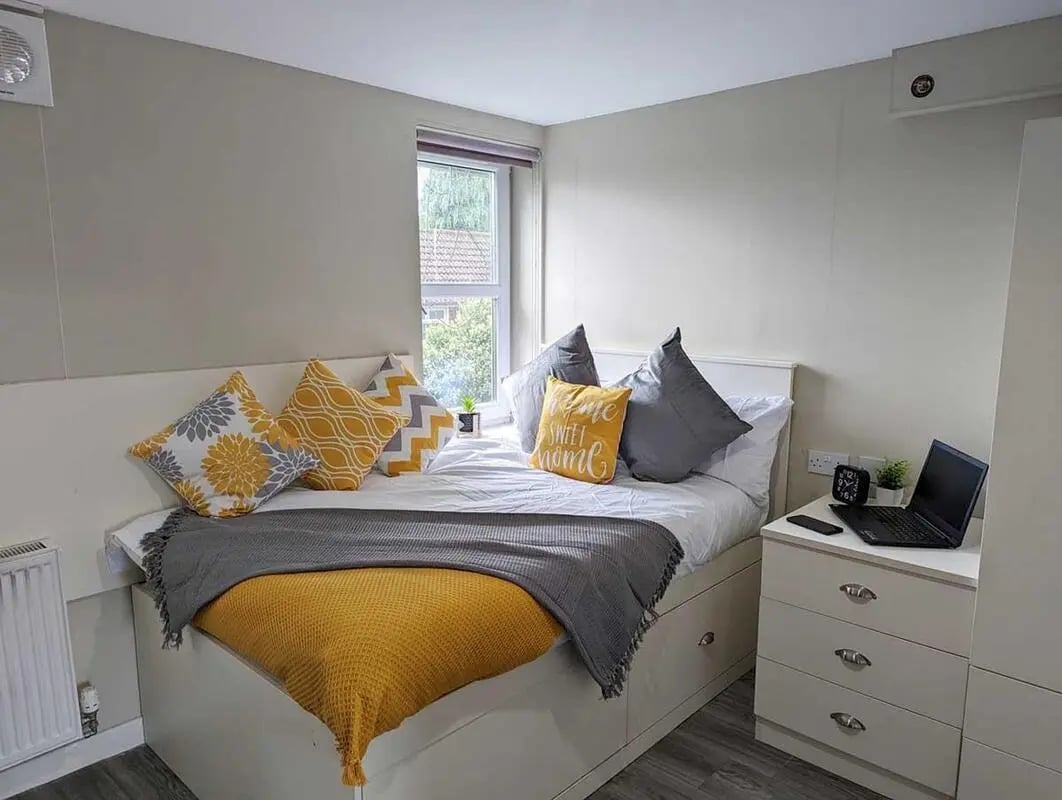 Bed with yellow pillows bedside table laptop bedroom at Peterson Hall in Dundee Student Accommodation