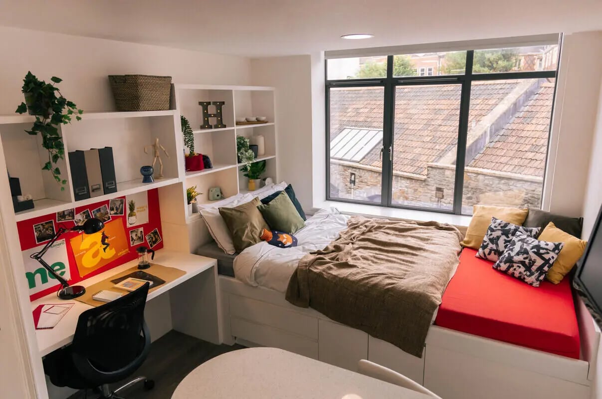 Desk plant bedding and red cushioned seating bedroom at Stonebridge House in Bristol Student Accommodation