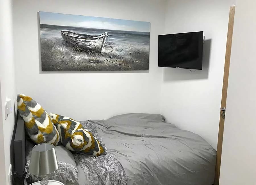 Bed with grey bedding patterned pillows painting and TV bedroom at The Student Block in Loughborough Student Accommodation