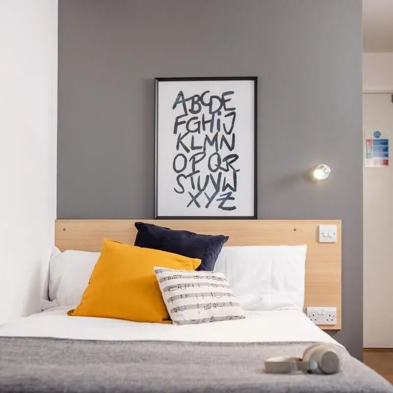 Bed with pillows artwork and headphones bedroom at Prince Consort Village in London Student Accommodation