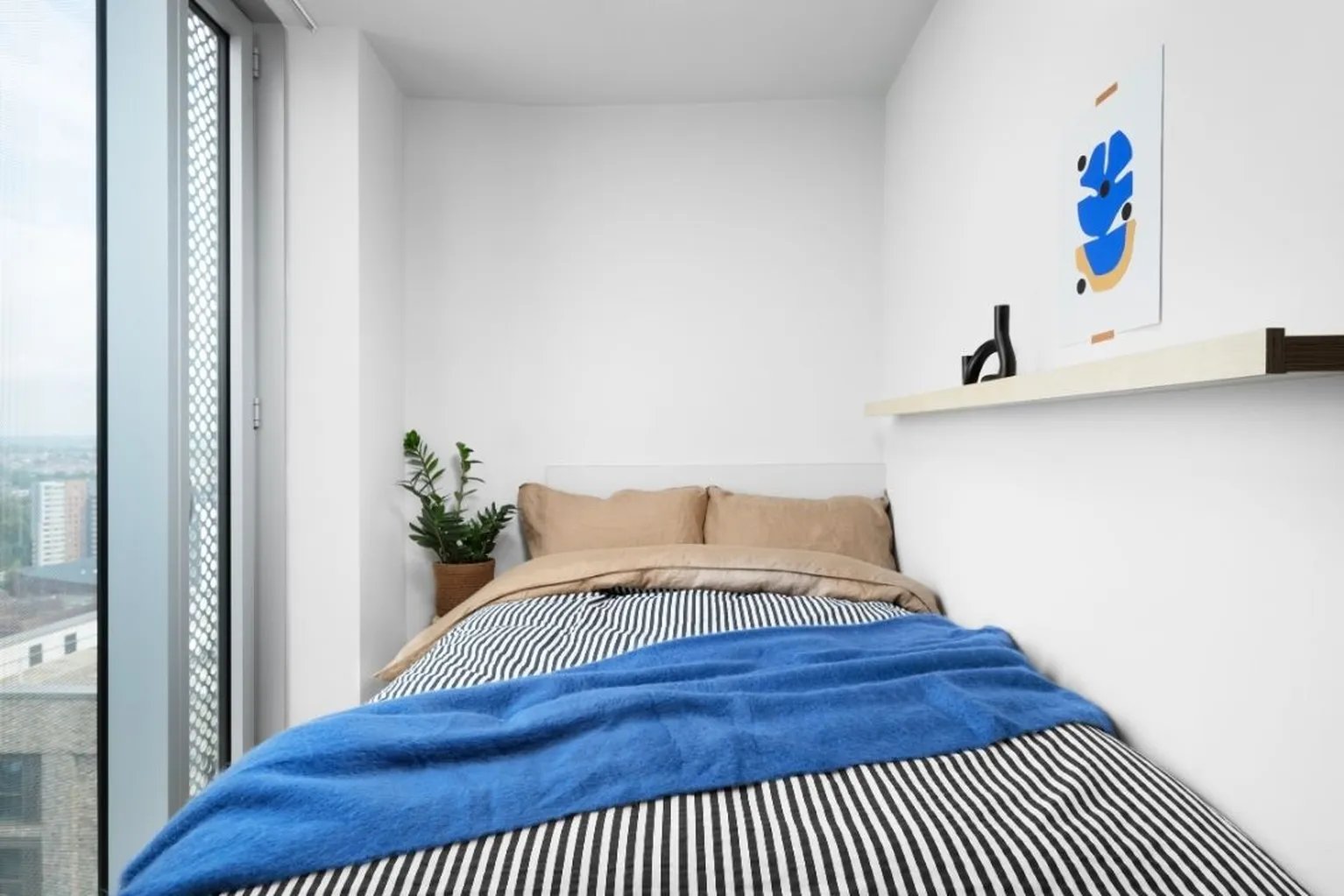 Bed with striped bedding blue throw plant art bedroom at Scape Leeds in Leeds Student Accommodation