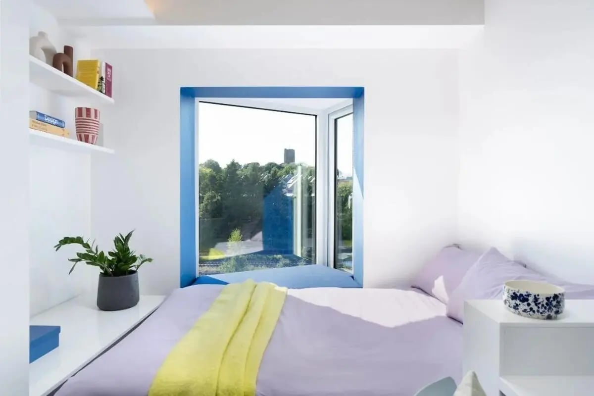 Bed with yellow blanket plant books bedroom at Scape Guildford in Guildford Student Accommodation