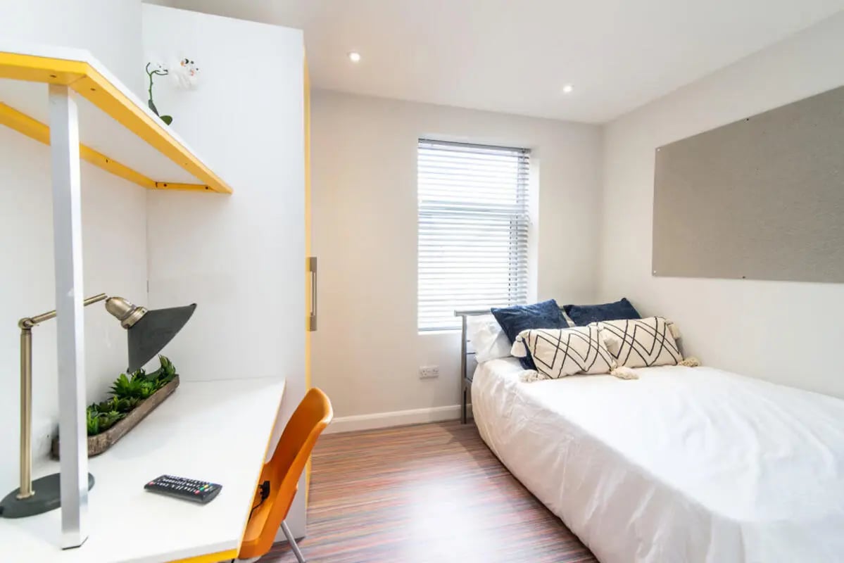 Desk lamp plant remote white bed blue pillows bedroom at 18 Cauldon Road in Stoke-On-Trent Student Accommodation