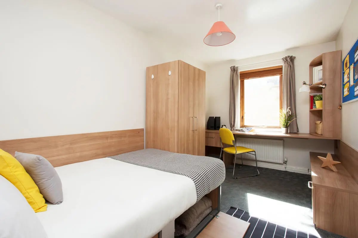 Bed desk wardrobe window yellow chair bedroom at Sunlight Apartments in London Student Accommodation