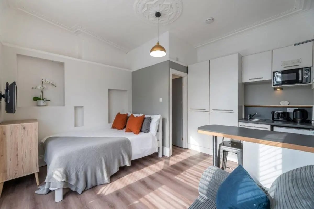 Bed with orange pillows kitchen area living room at 29 Trewhitt Road in Newcastle Upon Tyne Student Accommodation