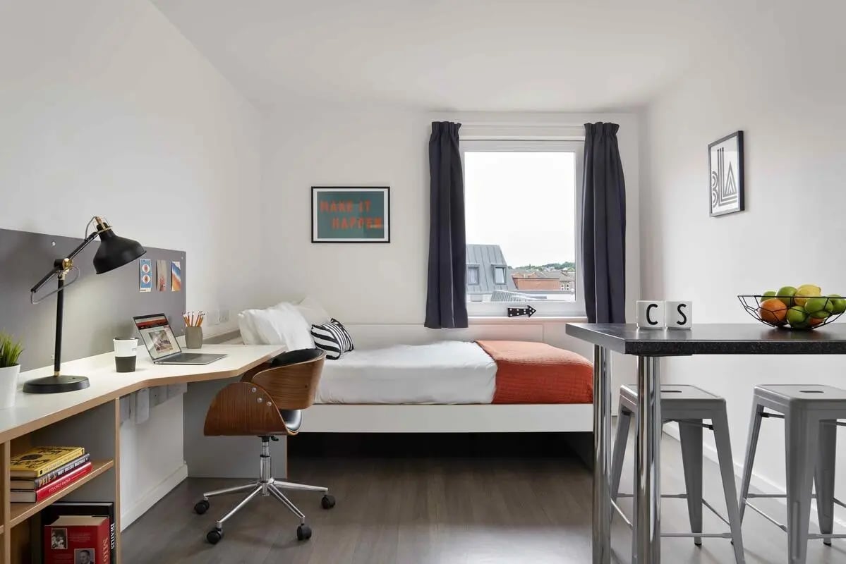 Desk bed table with stools and fruit bedroom at Asa Briggs House in Leeds Student Accommodation